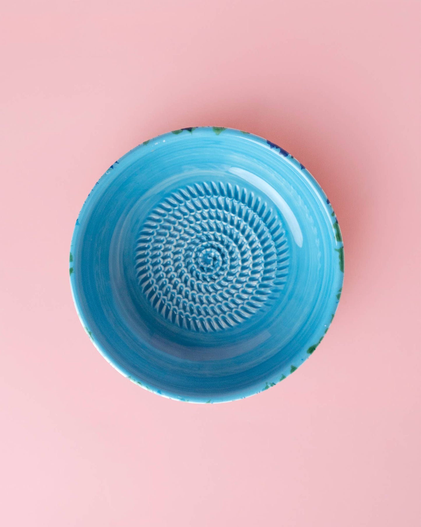 The Alfar Tierra Cocida Garlic Grater Plate - Medium Ceramic - Azul features a textured, spiral-patterned surface and is shown centered on a plain pink background in a top-down view.