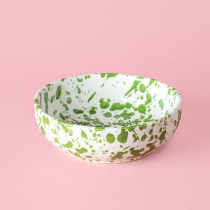 The Garlic Grater Plate - Medium Ceramic Green - Moss by Alfar Tierra Cocida is a handmade Spanish ceramic bowl with green splatters on white, shown on a light pink surface.
