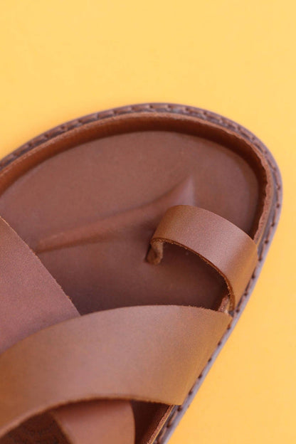 Close-up of Mexas EU’s Tampico sandals, handcrafted in brown with crisscross straps, showcased against a solid yellow background.